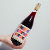 Bottle of Catch & Release Wine Anyone Anytime Anyplace, red blend, with a colorful label held by a hand on a light gray background
