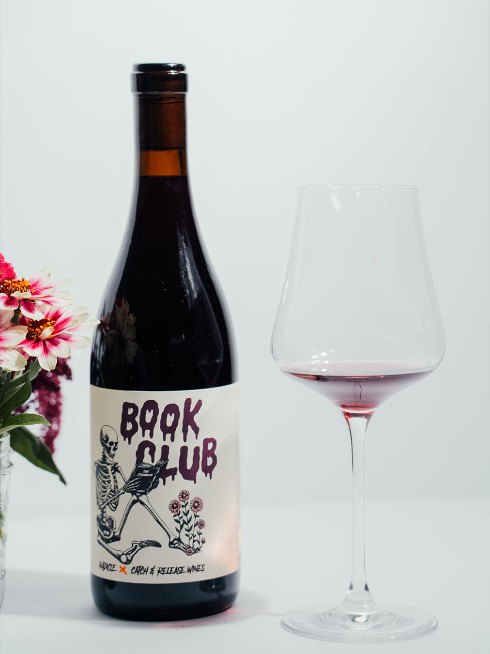 2024 Book Club bottle with a glass of red wine and flowers